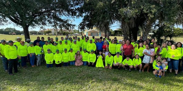 Large group wearing bright yellow shirts posing outdoors under trees.