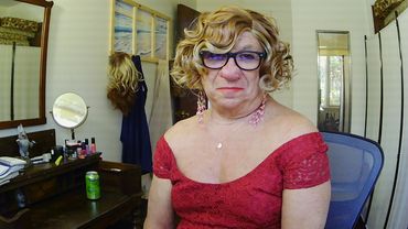 Person in red dress with curly blonde wig and glasses posing indoors.