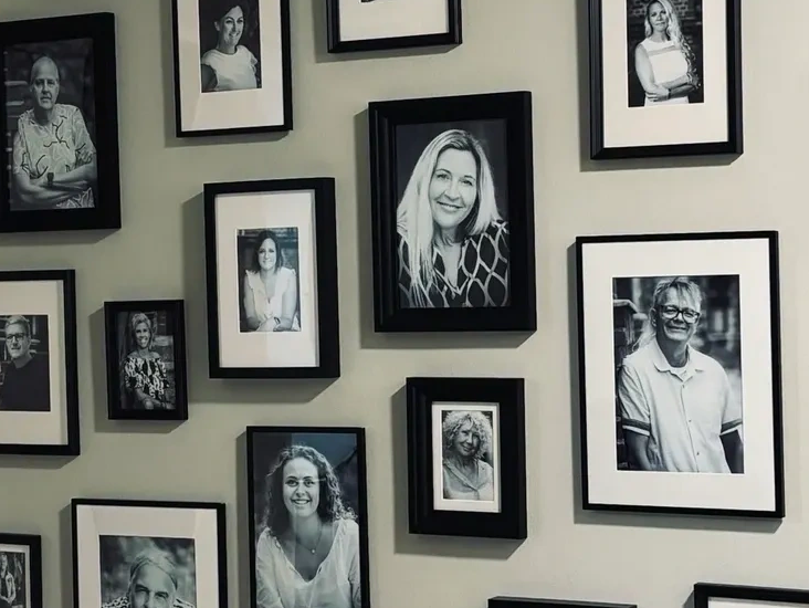 Porträtfotos von Teammitgliedern in schwarzen Bilderrahmen an einer Wand angeordnet.