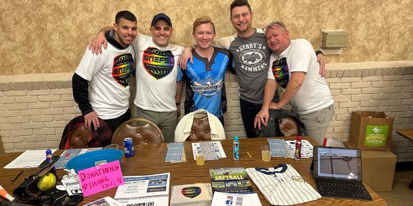 Five men stand behind a table with donation signs and materials, smiling at the camera.