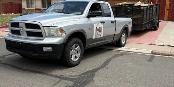 Silver Dodge Ram pickup truck with trailer parked on a residential street.