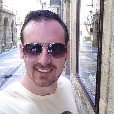 Man wearing sunglasses smiling in an urban alley.
