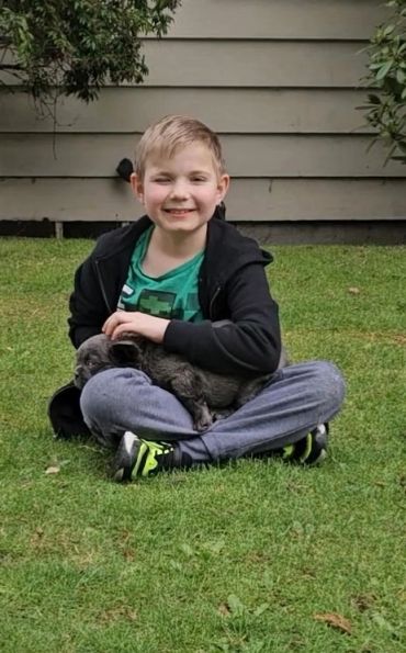 Boy sitting on grass holding a small dog, smiling.