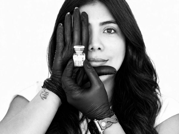Woman holding a small vial with black-gloved hands.