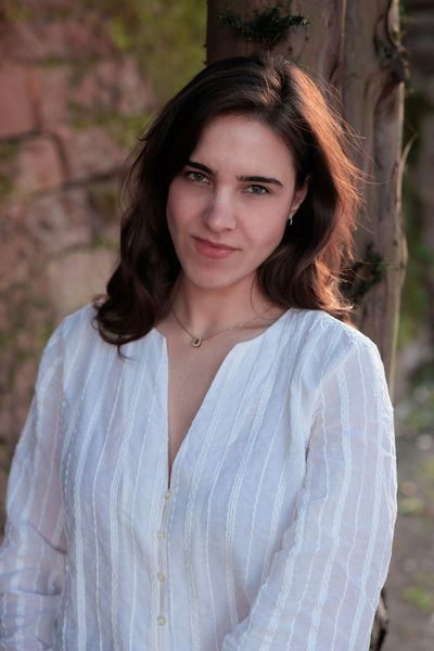 Young woman in a white blouse standing outdoors by a tree.