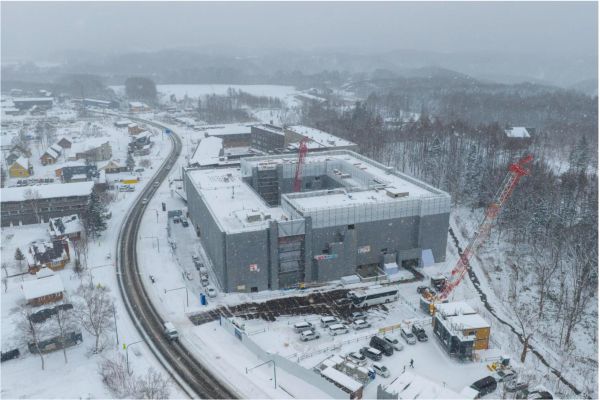 Snow-covered construction site of a large building near a curved road in a rural area.
