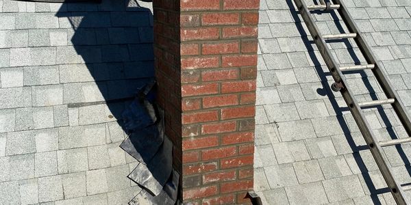 Brick chimney on a shingled roof with a ladder nearby.