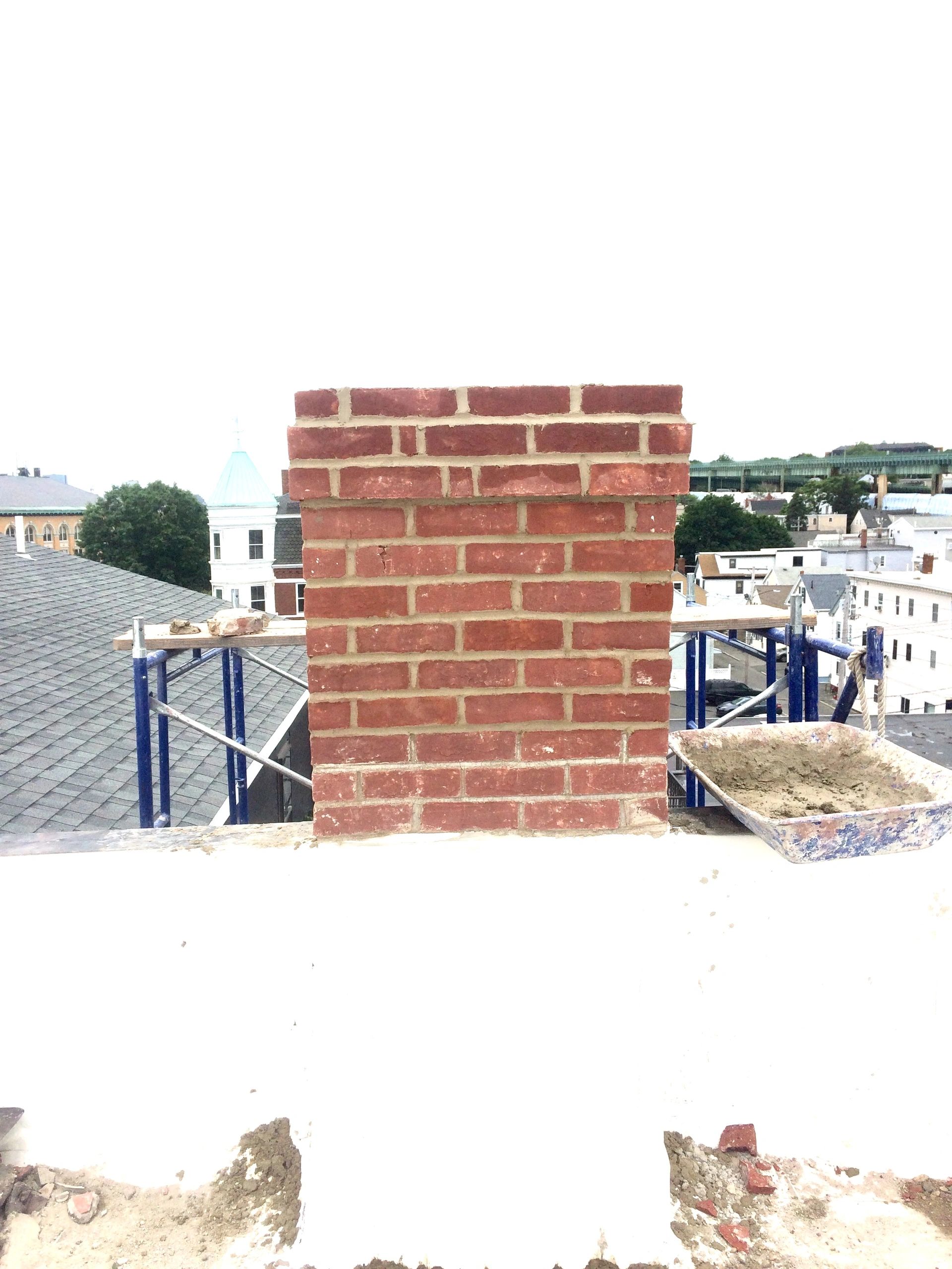 Freshly built brick chimney on a rooftop under construction.