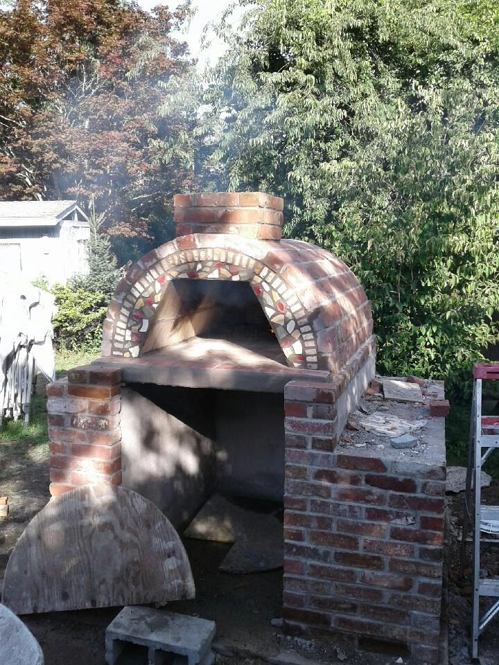 A brick outdoor pizza oven with mosaic decoration in a garden.