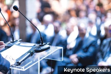 Microphones on a podium with an audience in the background preparing for a keynote speaker