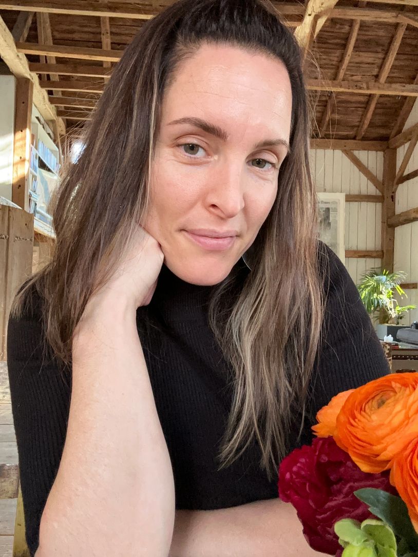 Woman with long hair in a black top sitting indoors with flowers.