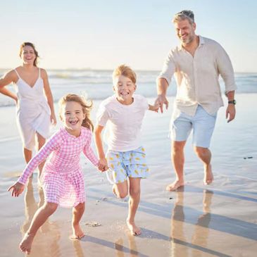 Happy family running barefoot on the beach at sunset.