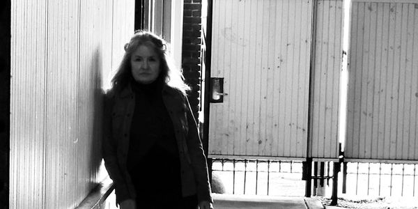 Woman standing in a dimly lit corridor with wooden walls and a closed gate.
