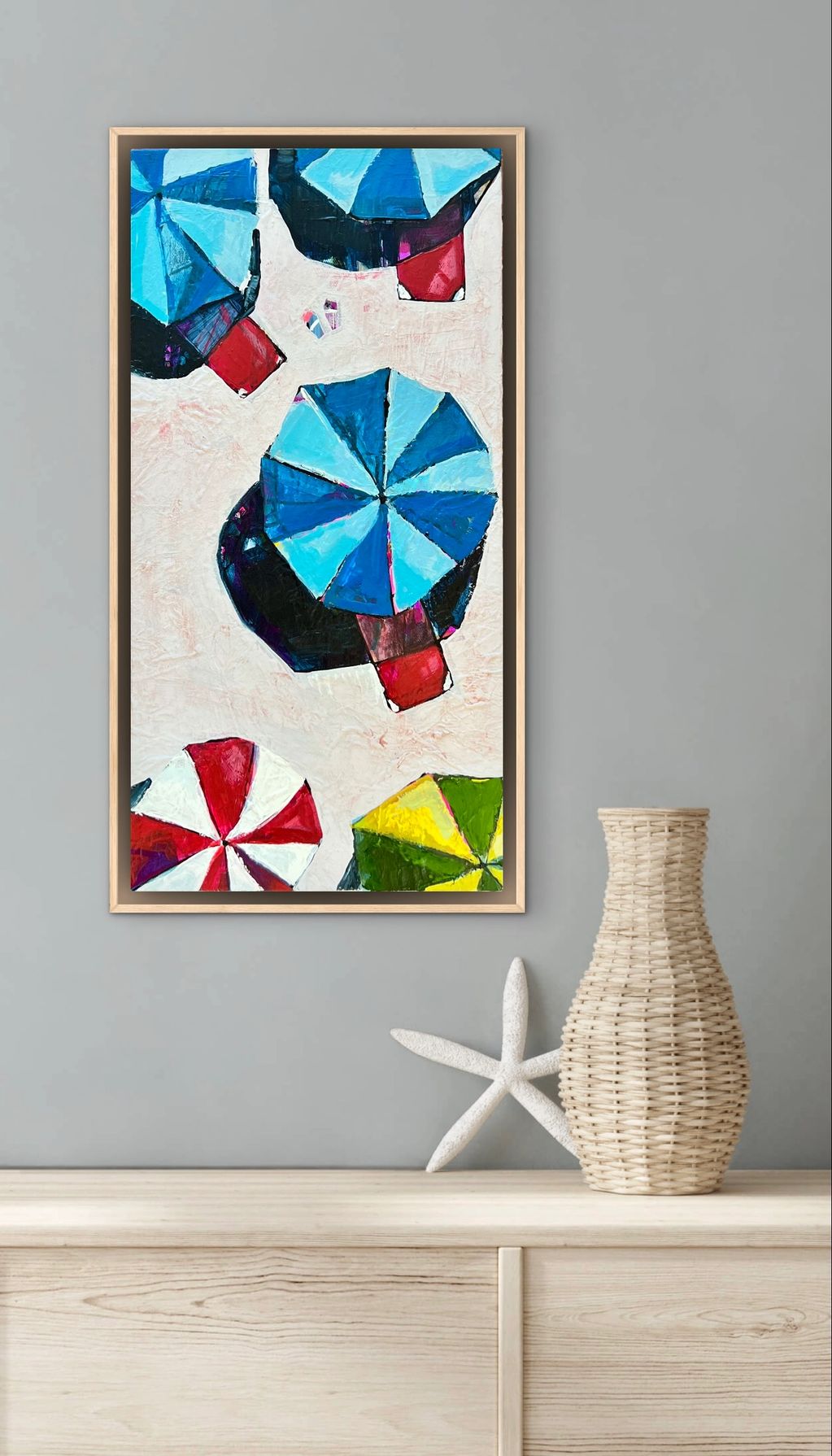 Colorful abstract painting of beach umbrellas in a wooden frame on a gray wall.
