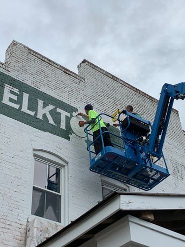 Jimmy on a forklift painting a large wall sign for Elkton Brewing Co.
