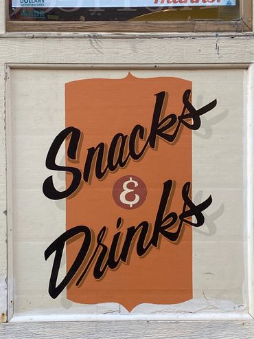 Wall sign with script writing that says "Snacks & Drinks."