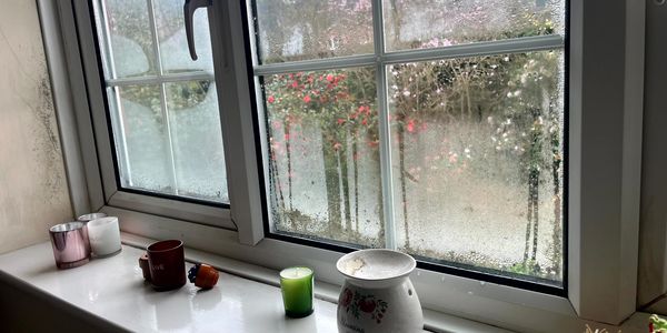 A foggy window with candles and a decorative jar on the sill.