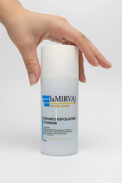A hand holds a LA MIRVAJ Advance Exfoliating Cleanser bottle against a white background.