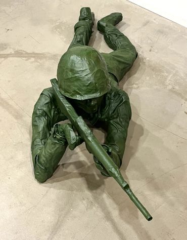 Green soldier statue lying prone with a rifle on the floor.