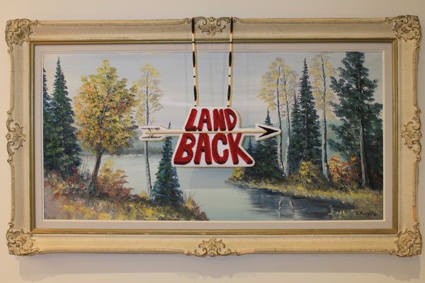 ornately framed landscape painting with a beaded medallion reading "LAND BACK" with an arrow draped 