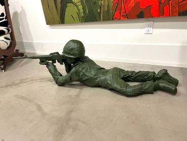 Green toy soldier lying prone aiming a rifle on the floor.