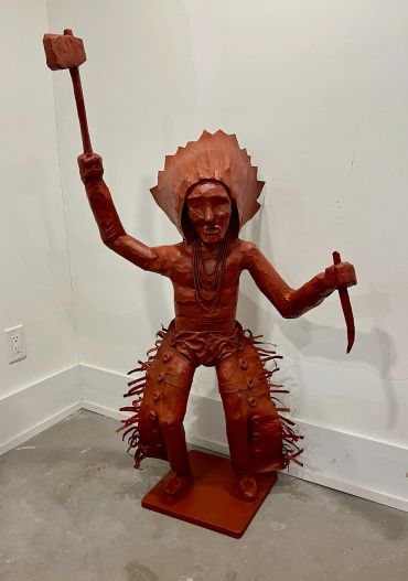 Red warrior statue holding a club and dagger in a fierce pose.
