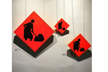 Diamond shaped orange construction sign. Figure of a priest wearing a cassock with a shovel digging.