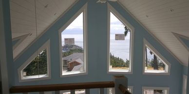 A cozy room with triangular windows overlooking the ocean and trees.