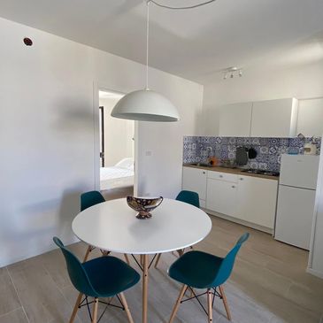 Modern white kitchen with round table and blue chairs.