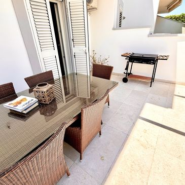 Outdoor patio with wicker chairs, glass table, and a barbecue grill.