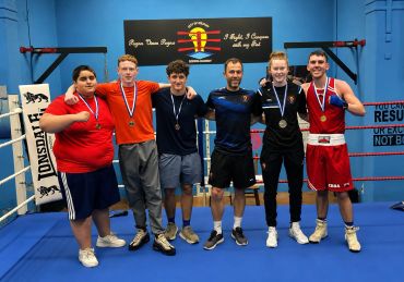 Six people posing in a boxing ring with medals.