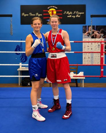 Two female boxers posing in a boxing ring with medals.