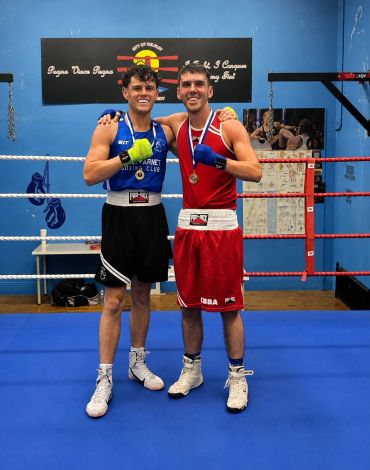 Two smiling boxers posing with medals in a boxing ring.