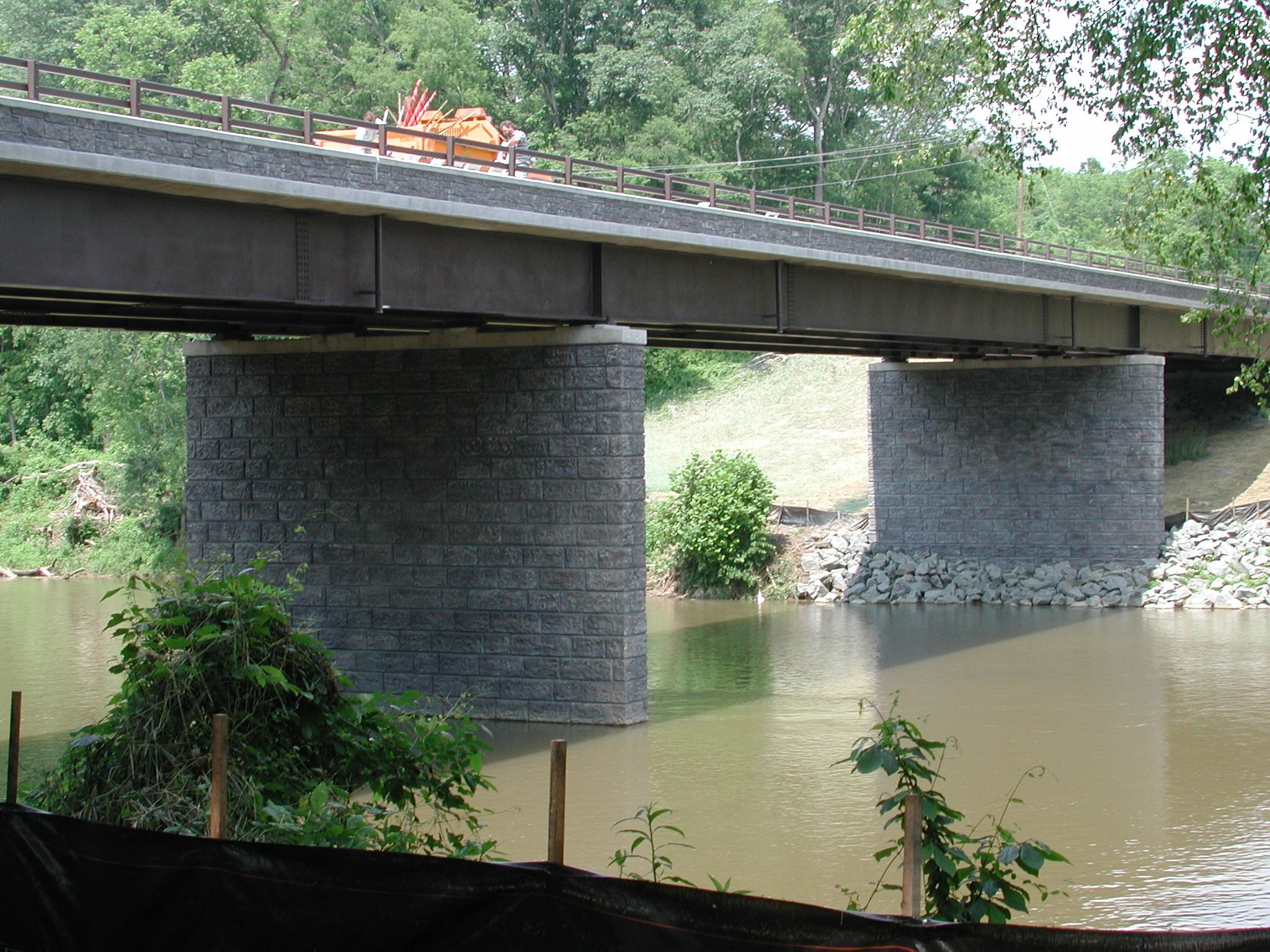 A concrete and steel bridge over a river with greenery.
