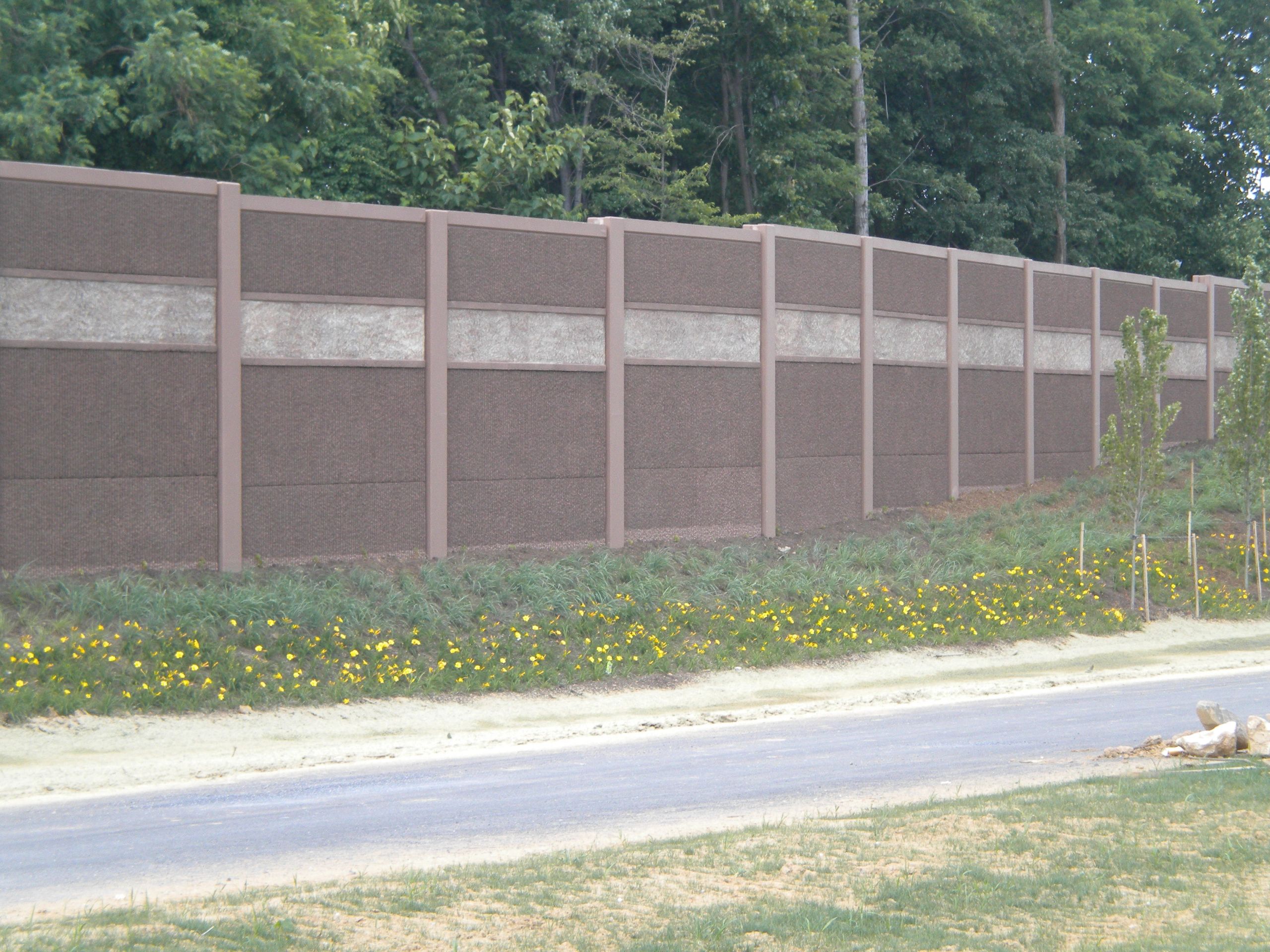 Long noise barrier wall beside road and greenery.