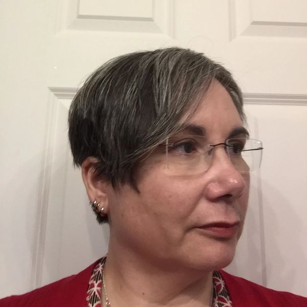Profile of a woman with short salt-and-pepper hair and glasses.