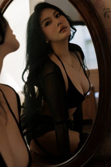 Woman in black lingerie posing in front of a mirror.