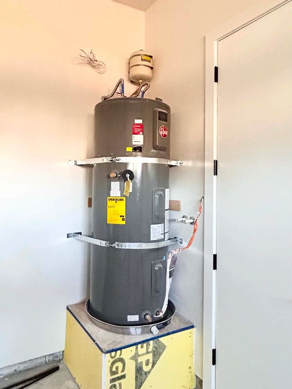 A secured gray water heater installed on a yellow base in a corner.