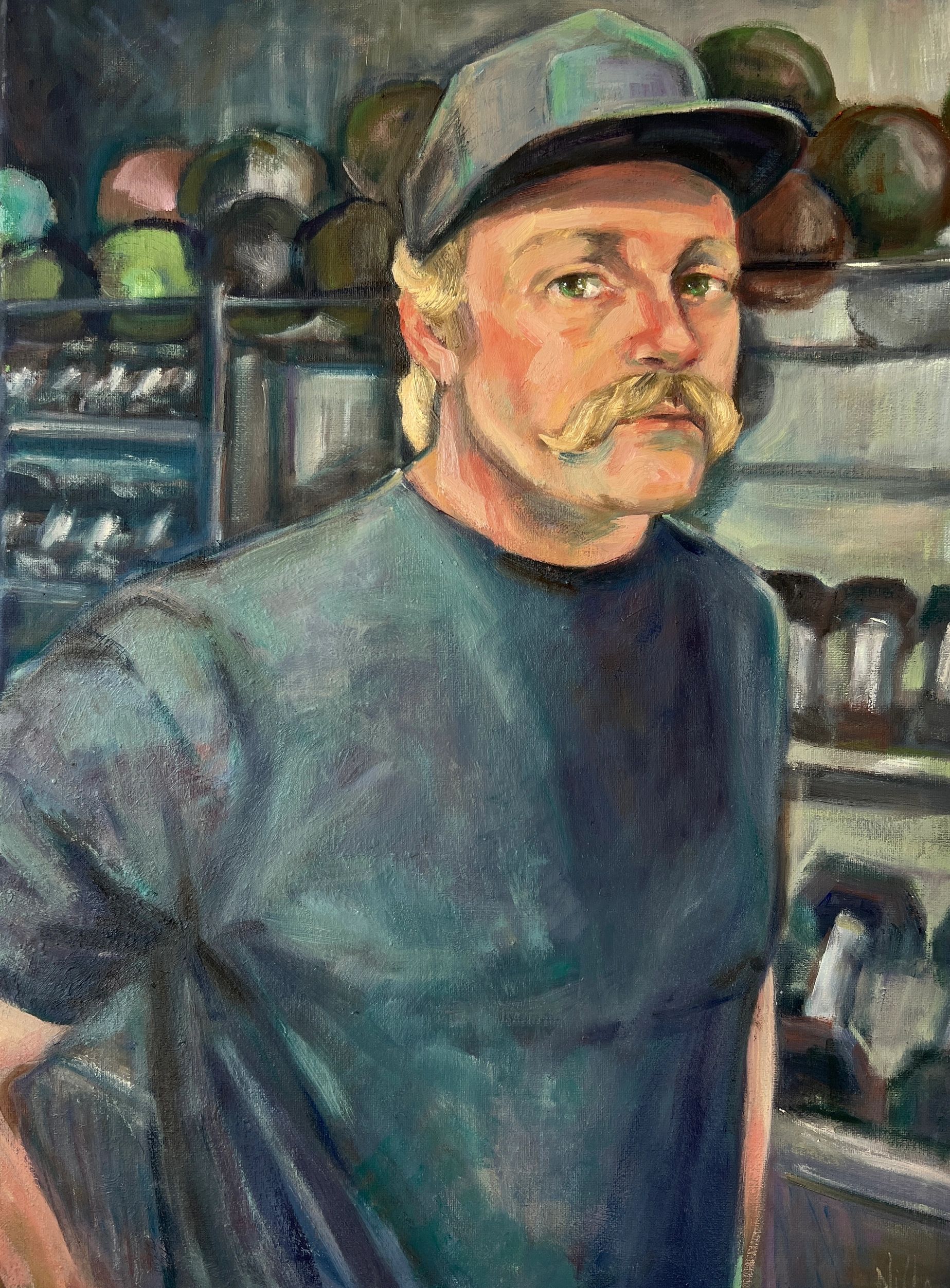 A man with a mustache and cap stands in a shop with hats.