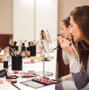 Woman applying makeup in front of a mirror with makeup tools around.