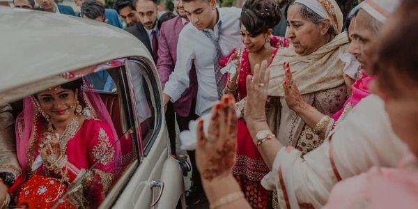 Bride in red lehenga waving goodbye as she leaves in a car.