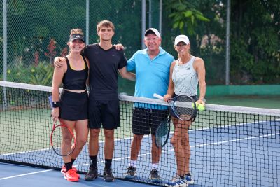 Group of four standing on a tennis court with rackets.