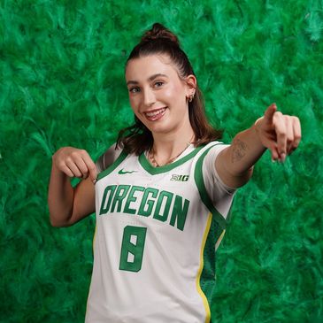 Female basketball player in Oregon jersey pointing at it with a smile.
