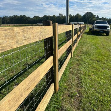 Wood and wire fence along a grassy area with a truck.