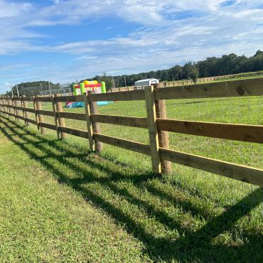 Wooden fence casting long shadows on a grassy field.