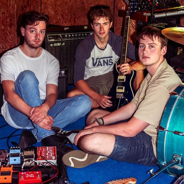 Three young men with musical instruments and pedals in a practice space.