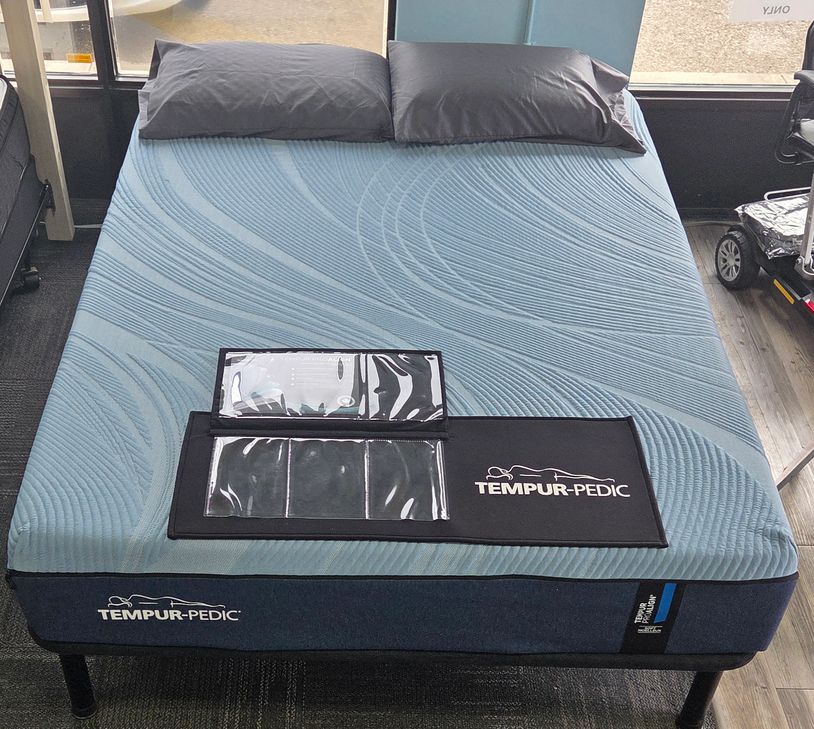 Tempur-Pedic mattress with blue cover and two pillows on a bed frame.
