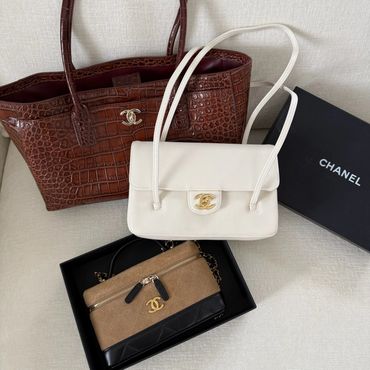 Three Chanel handbags with box on a beige surface.