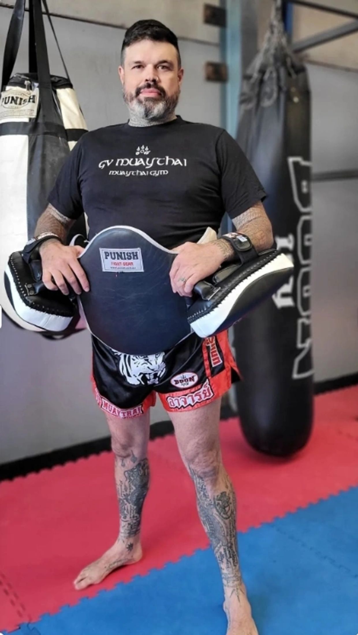 Man in Muay Thai training gear holding pads in a gym.