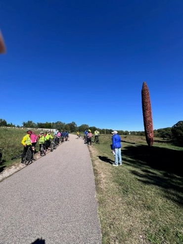 Group of cyclists pausing on a path near a tall sculpture.